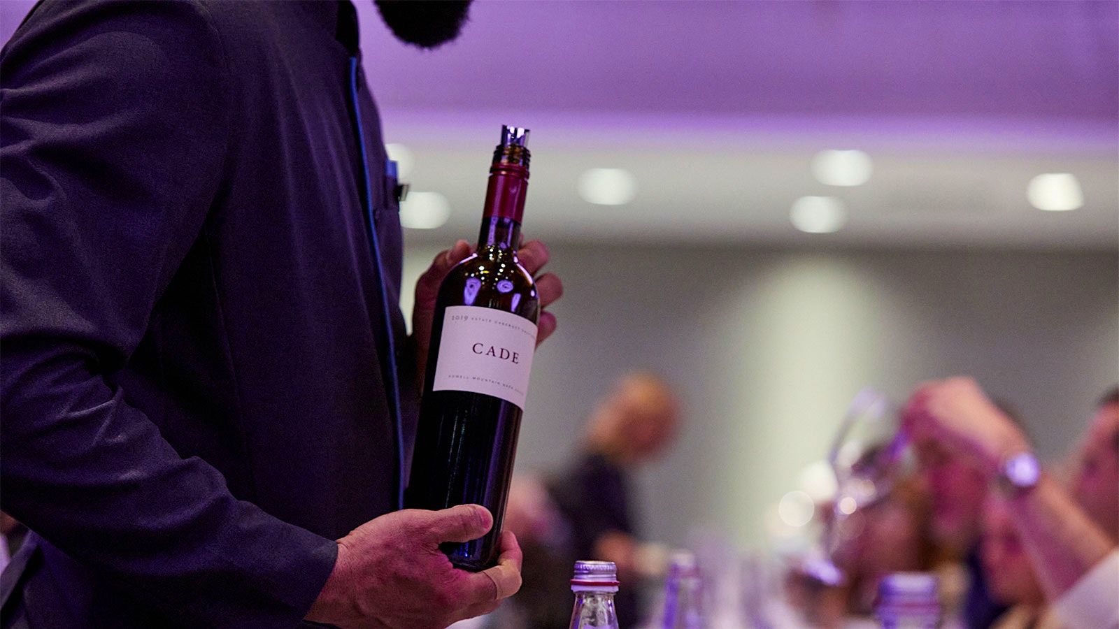 A Wine Experience staff member pouring a bottle of Cade's Cabernet Sauvignon Howell Mountain 2019 for guests